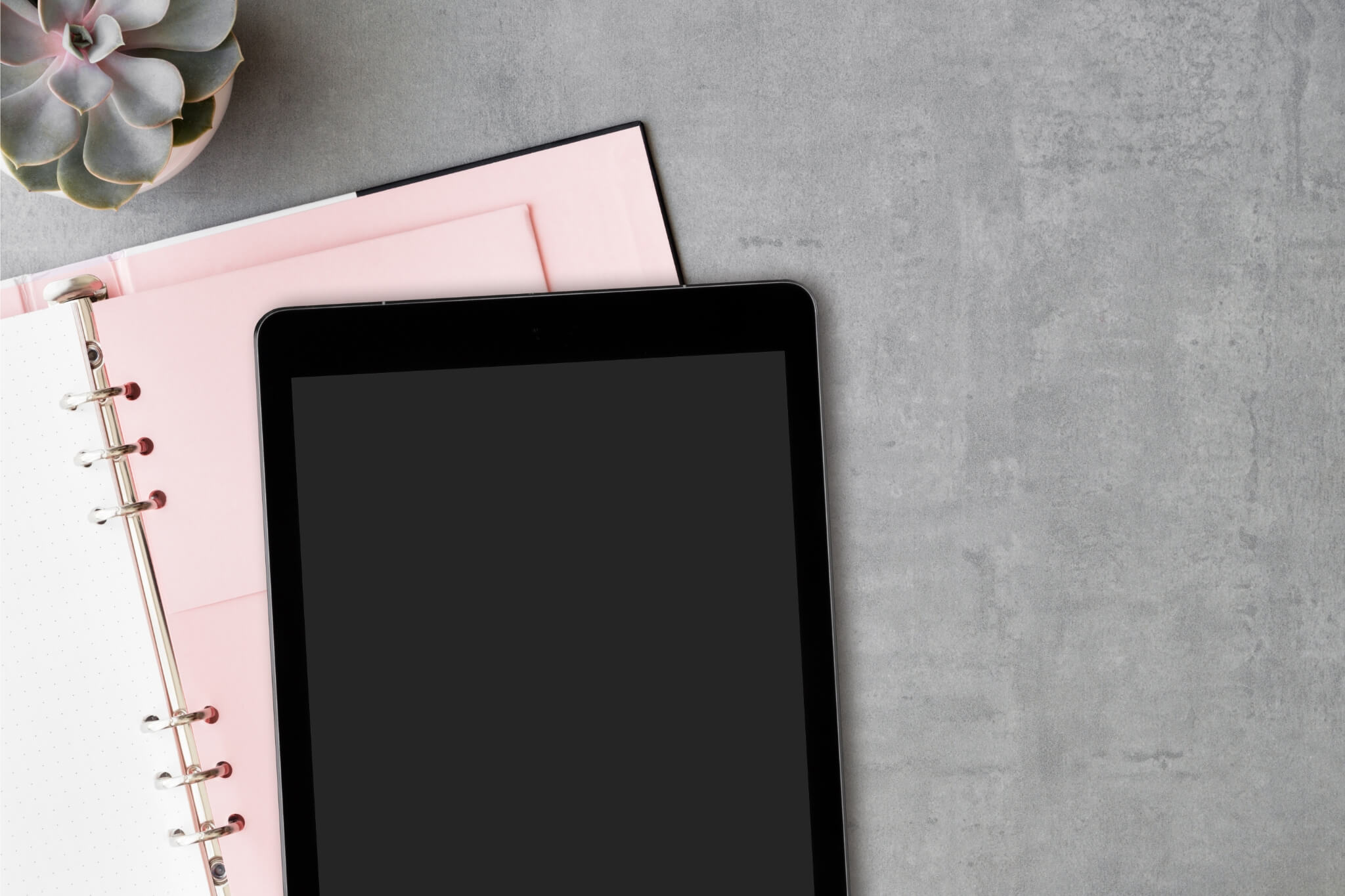 Tablet on top of a feminine and delicate pink agenda and an artificial plant