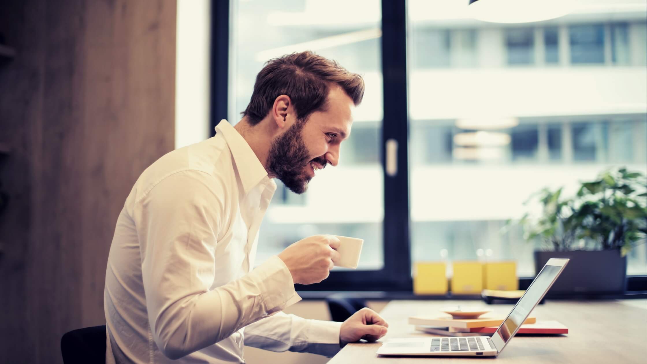 Business man with a white mug in his hand checking his mails and smiling