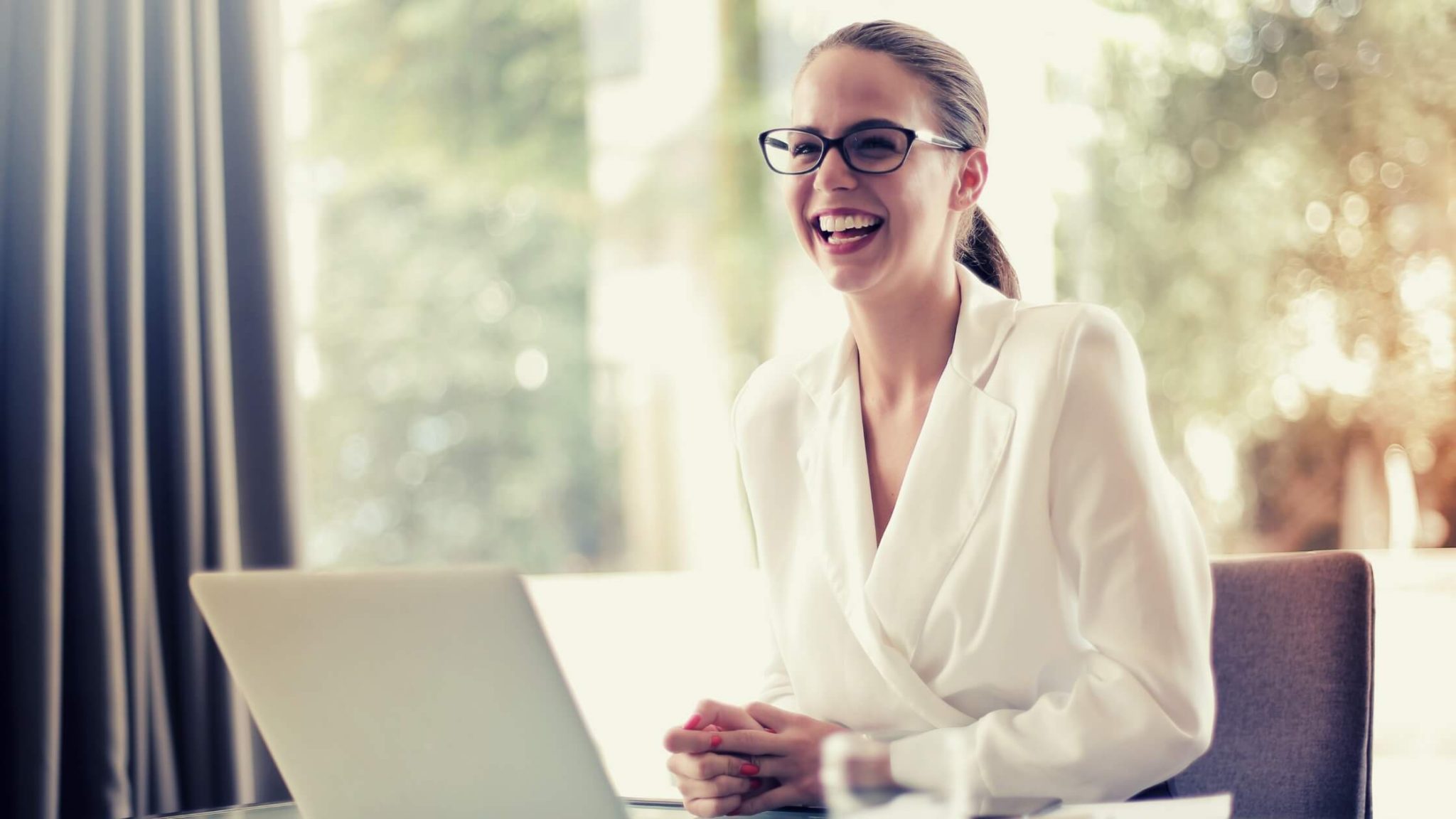 elegant woman with glasses smiling in front of a laptop