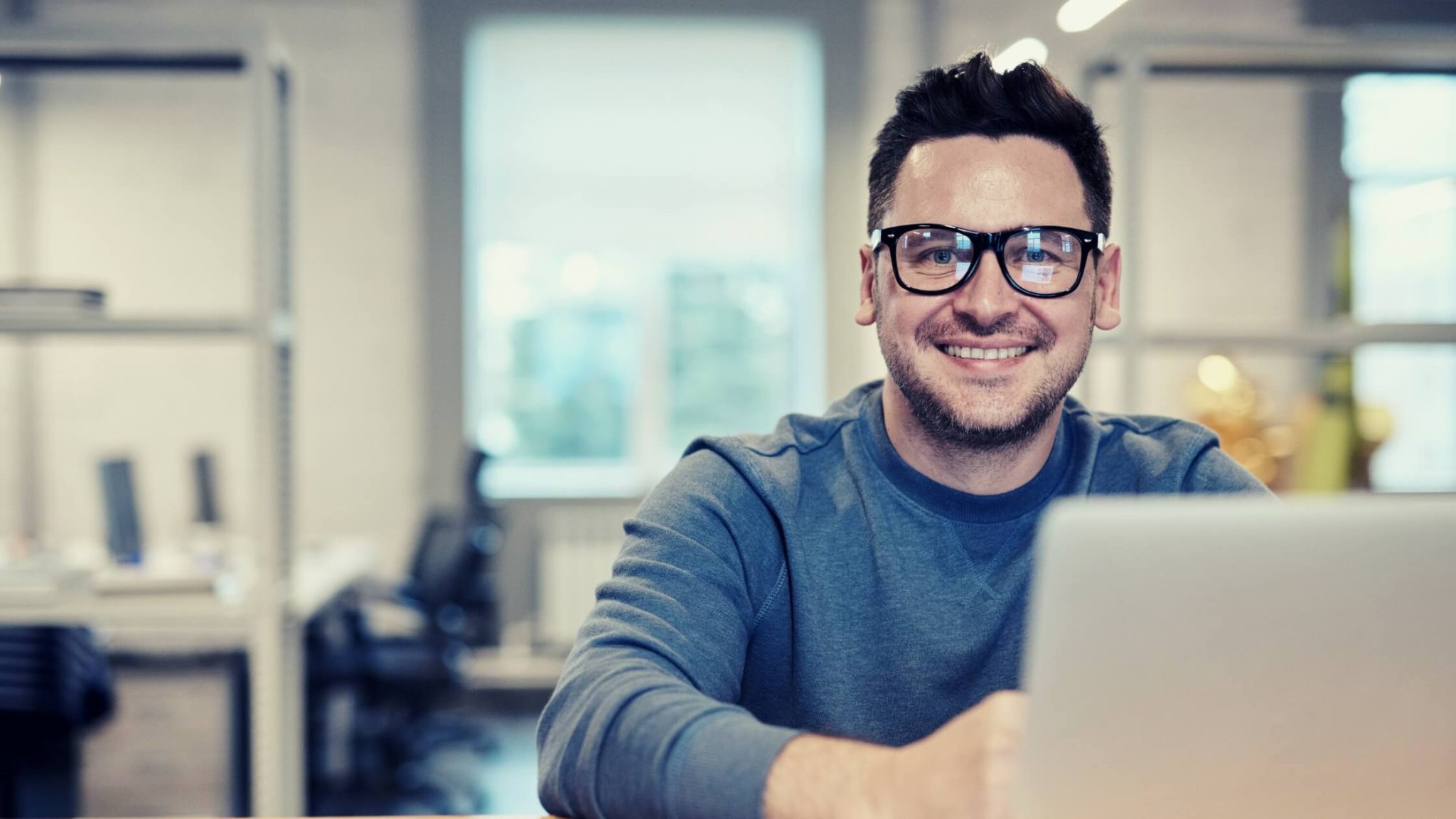 Man with glasses working on his laptop and smiling