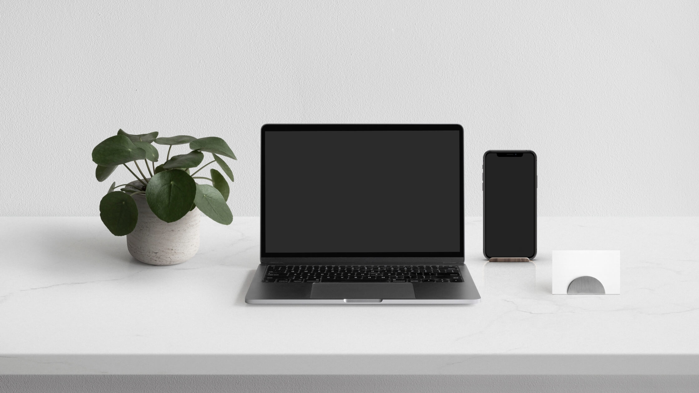 elegant and minimalist workstation with an artificial plant, a laptop, a cell phone, and business cards