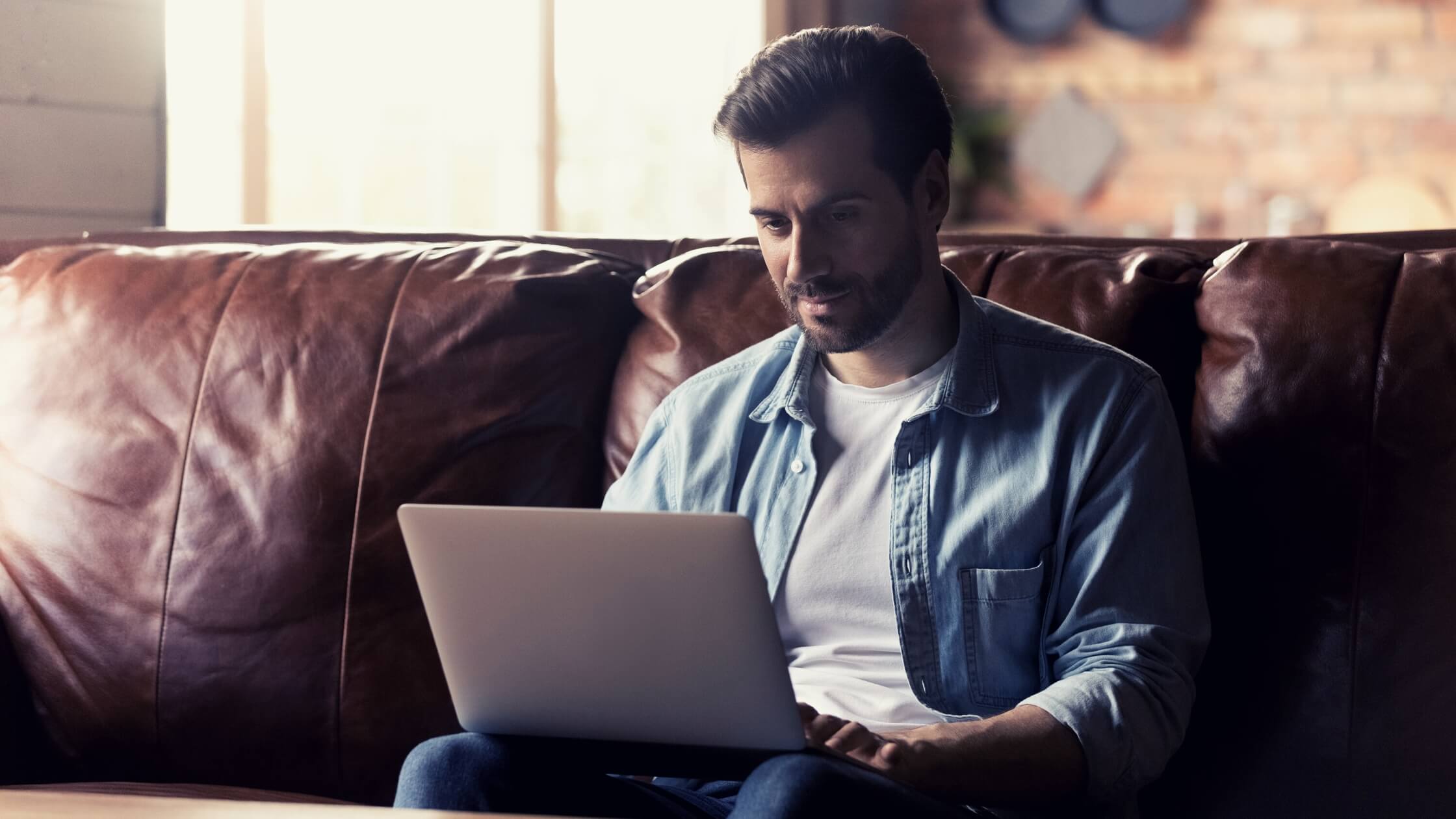 a remote worker sitting on a couch working on his laptop