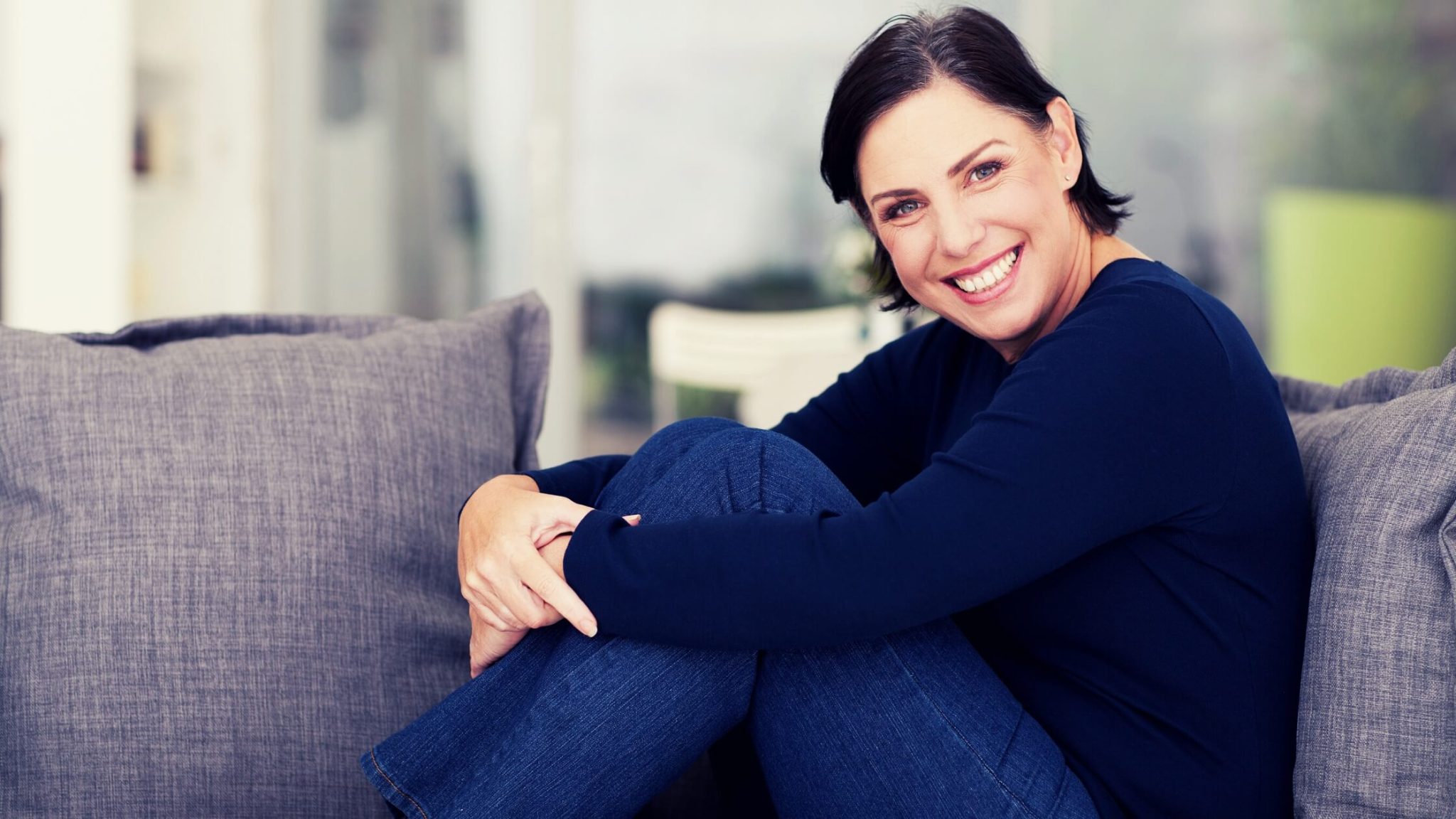 Smiling professional woman sitting comfortably at home, representing confidence and support in marketing for coaches